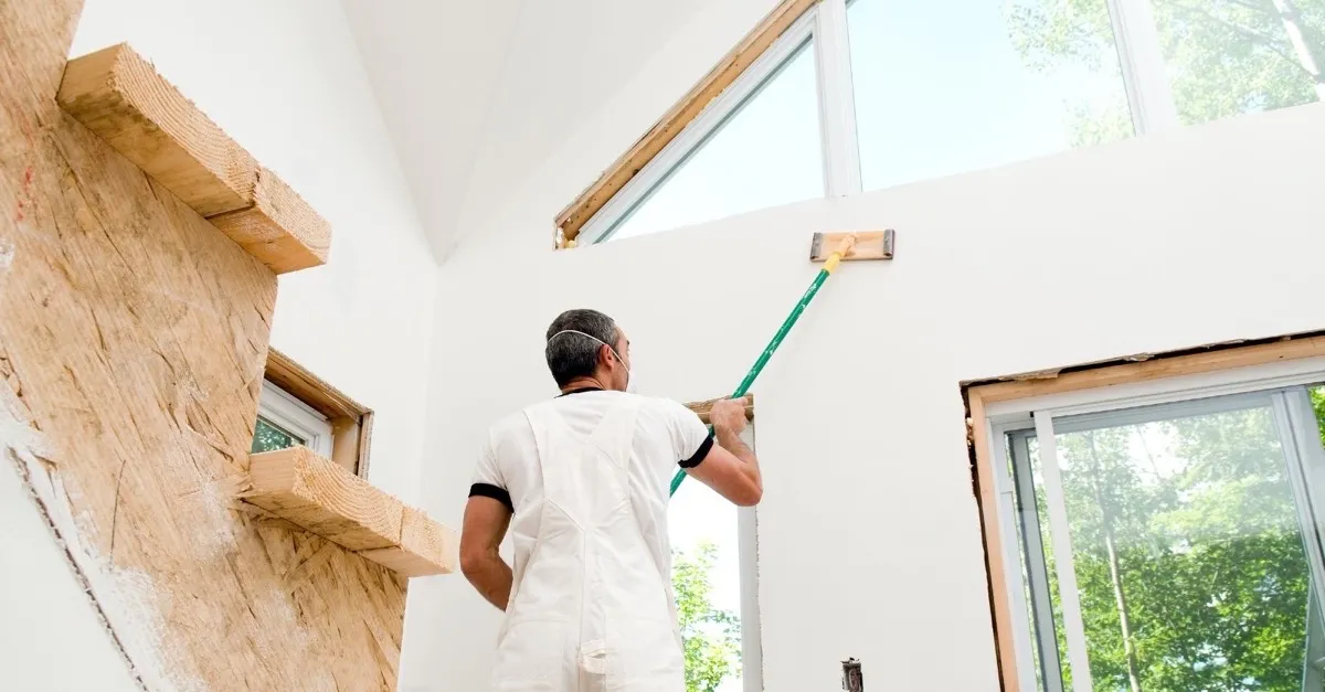 A finisher sanding a tall, paint-ready Level 4 wall in a bright room